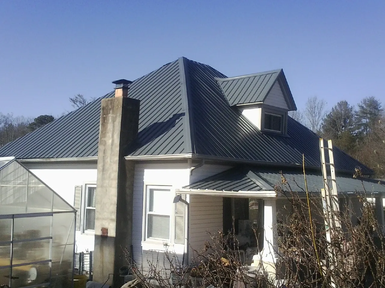 Dark blue standing seam metal roof on a white farmhouse with dormer — Slate & Tile Roof Repair by Roofing Brothers in South Rockwood