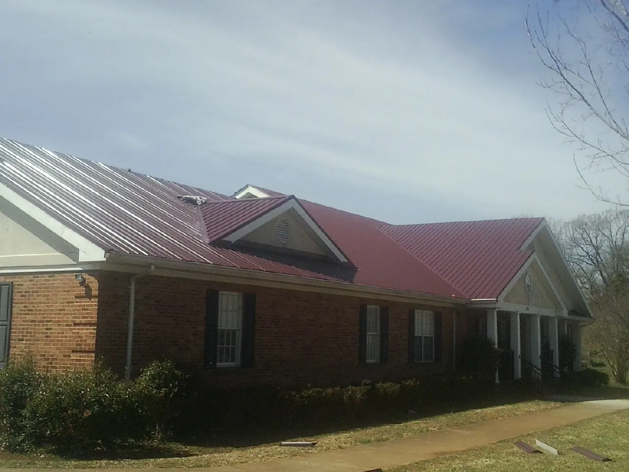 Red metal roof with gabled entries on a long brick building, from a Hail Damage Roof Repair job in South Rockwood