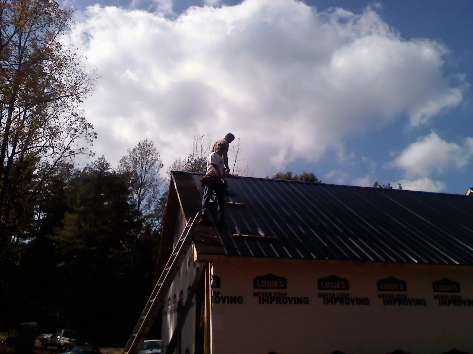 Roofer fastening dark metal panels high against a cloudy sky, from a Roof Inspection job in South Rockwood
