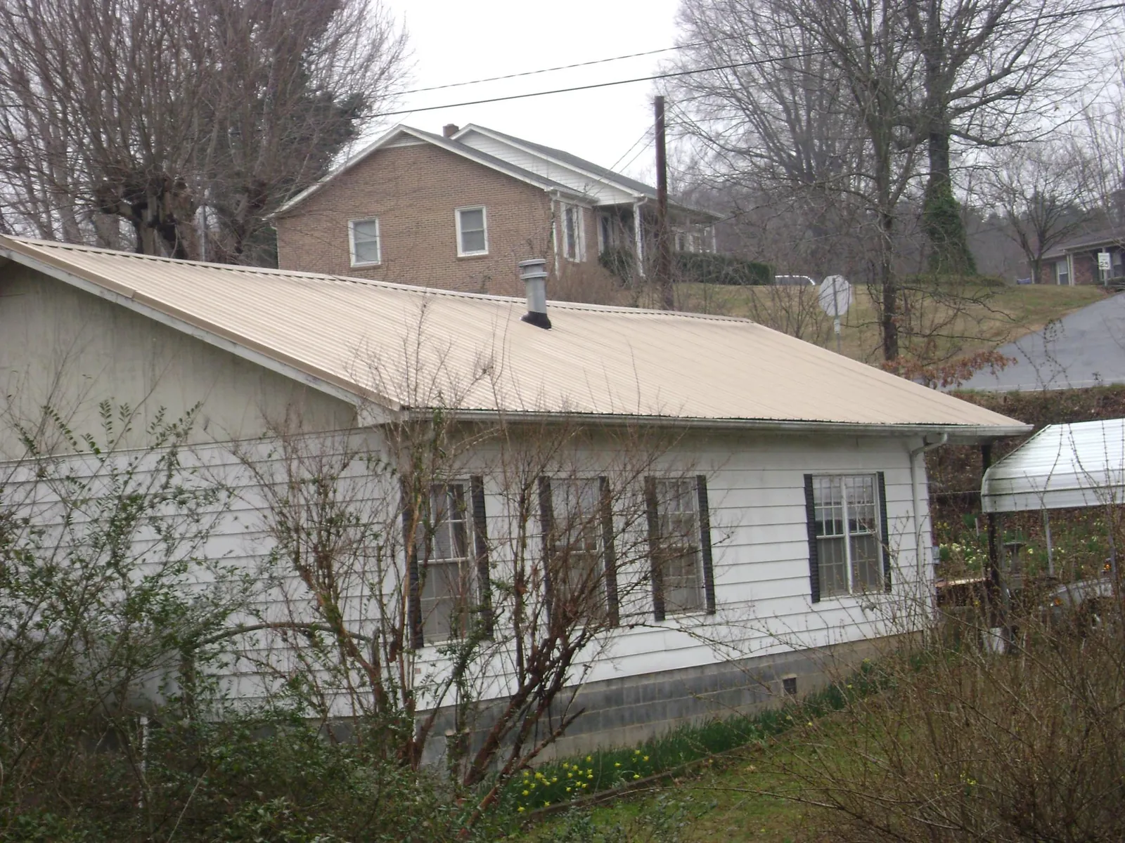 Tan metal roof on a white sided house set into a hillside — Commercial Roofing by Roofing Brothers in South Rockwood
